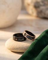 Black and rose gold Al Rayan smart tasbih rings resting on a stone beside green velvet