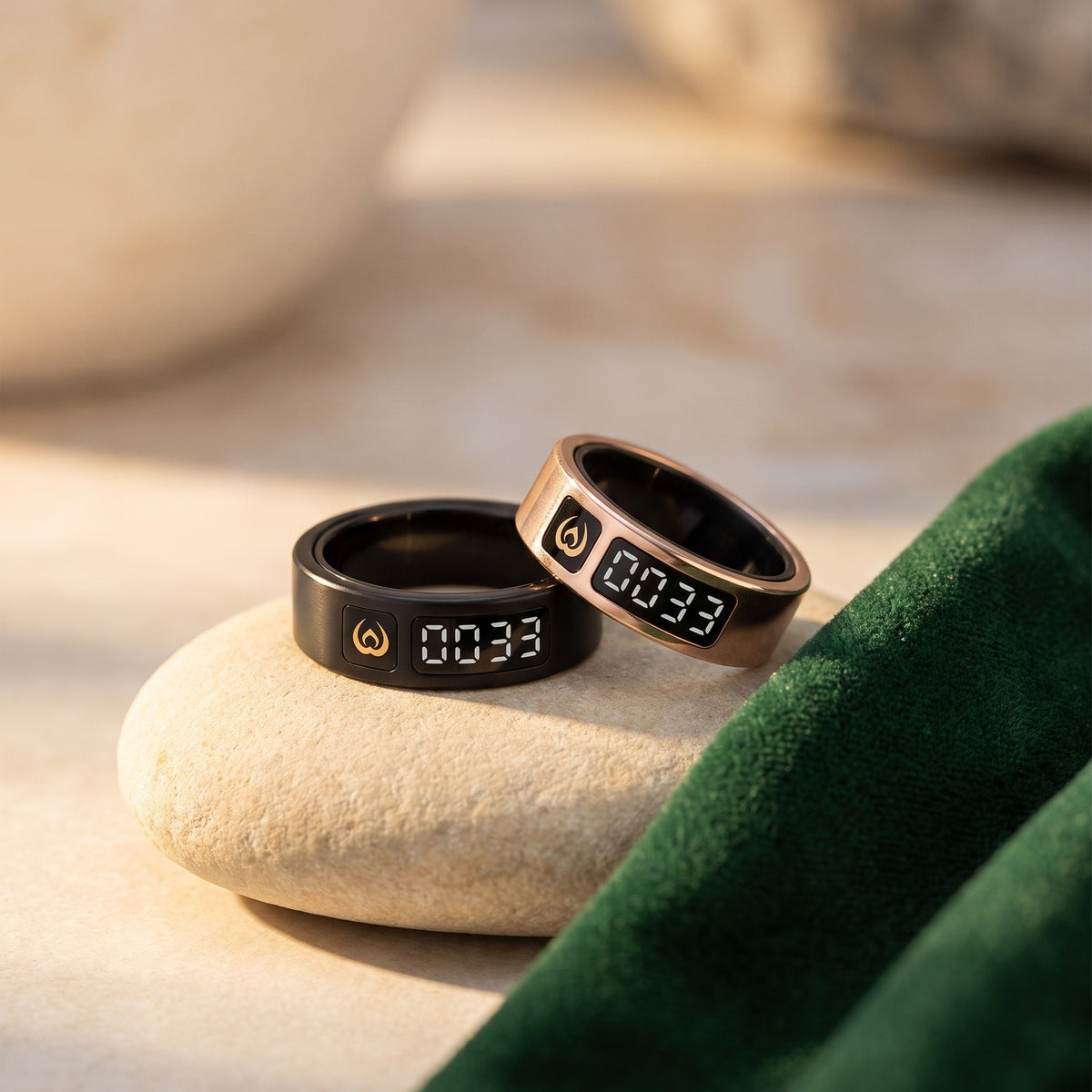 Black and rose gold Al Rayan Dhikr Rings resting on a stone beside green velvet